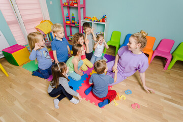 Preschool teacher teaching group of children, sitting on a floor