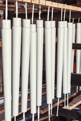 Collection of new wooden furniture legs drying after applying paint leaned on large rack in light woodwork shop close view
