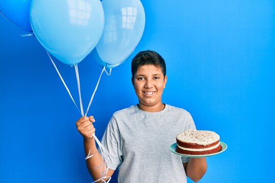 Teenager hispanic boy celebrating birthday with cake holding balloons smiling with a happy and cool smile on face. showing teeth.