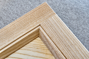 Stylish new detail of furniture facade made of light veneer and solid textured ash wood on gray textile background close view