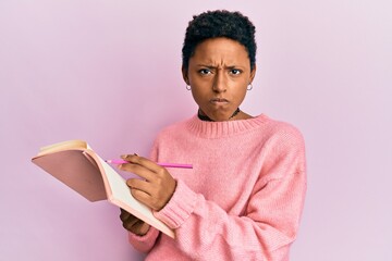 Young african american girl reading and writing book skeptic and nervous, frowning upset because of...