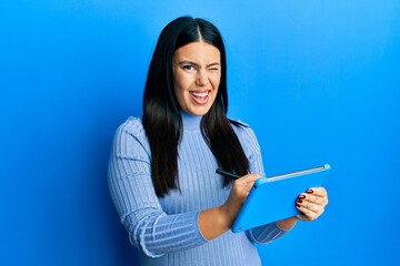 Obraz premium Beautiful brunette woman using touchpad drawing on screen winking looking at the camera with sexy expression, cheerful and happy face.