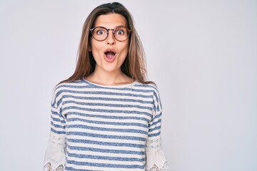 Beautiful caucasian woman wearing casual clothes and glasses scared and amazed with open mouth for...
