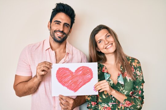 Beautiful young couple together holding heart draw smiling with a happy and cool smile on face. showing teeth.