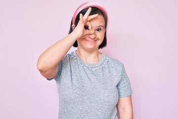 Brunette woman with down syndrome wearing casual clothes smiling happy doing ok sign with hand on eye looking through fingers