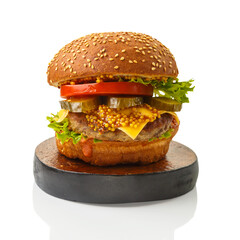 Classic burger with beef, cheese vegetables in sauce on a bun with sesame seeds on a wooden round stand on a white plate.