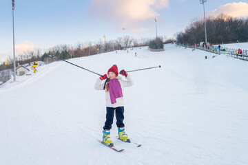 A little girl stands on skis swinging sticks. The child went skiing down the snowy slope. Active winter recreation concept