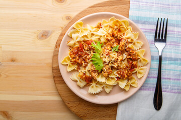 Pasta in tomato bolognese sauce in a plate on a wooden table on a napkin next to a fork. copy space