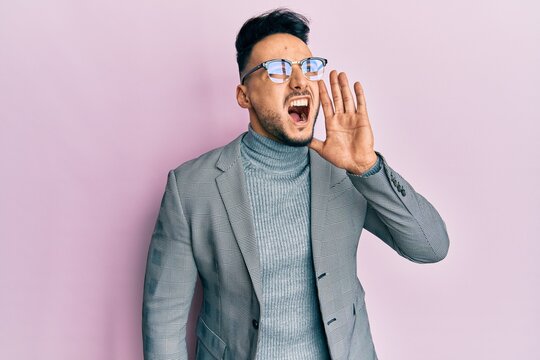Young arab man wearing business clothes shouting and screaming loud to side with hand on mouth. communication concept.
