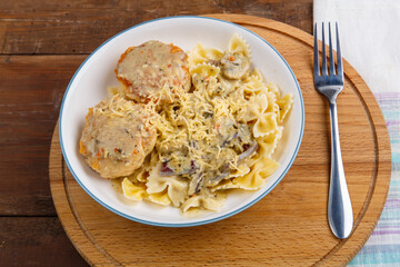 Pasta in a creamy sauce with mushrooms and chicken meatballs in a beige plate on a wooden table on a round stand with a fork