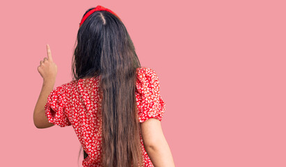 Brunette teenager girl wearing summer dress posing backwards pointing ahead with finger hand