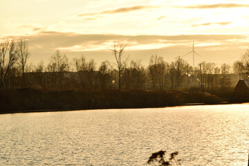 A pond in fall with a renewable energy windmill in the background