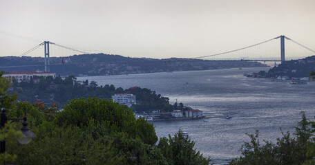 Naklejka premium Bosporus Bridge and Maidens tower are in the same frame. Sea traffic in Istanbul strait. Maiden tower under the leg of Bosporus Bridge. Sunset time in Istanbul.