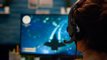 Over the shoulder pro gamer woman playing computer FPS shooter video game on championship, talking into headset . Cyber performing on powerful computer in stylish room during gaming tournament © DC Studio