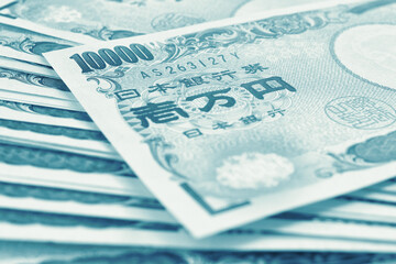 Obraz premium Light background on the theme of Japanese money, finance and economy. Blue green tinted backdrop. Yen banknotes close up. Blurred with focus on 10,000. Banking, savings, deposit and loan. Macro