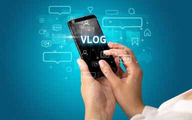 Female hand typing on smartphone with VLOG inscription, social media concept