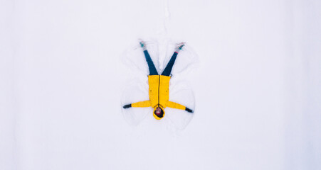 From above of happy carefree female in winter coat lying on white snow surface making angel and laughing during xmas vacation free time, woman doing childhood activities in Christmas Holidays
