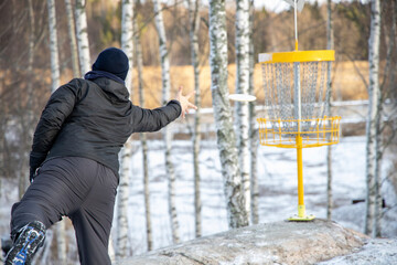 Disc golf player is putting to yellow basket on winter.