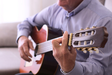 Concept music. Closeup of guitar and hands of a 60 year-old man playing guitar sitting.