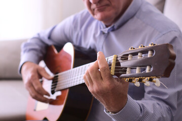 Concept music. Closeup of guitar and hands of a 60 year-old man playing guitar sitting.