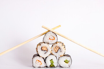 Eating Sushi with chopsticks. Sushi roll japanese food in restaurant isolated on white background. Fresh hosomaki pieces with rice and nori. Closeup of delicious japanese food with sushi roll.