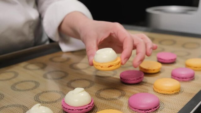 Pastry chef is filling cream chocolate macarons with pastry bag, close up.