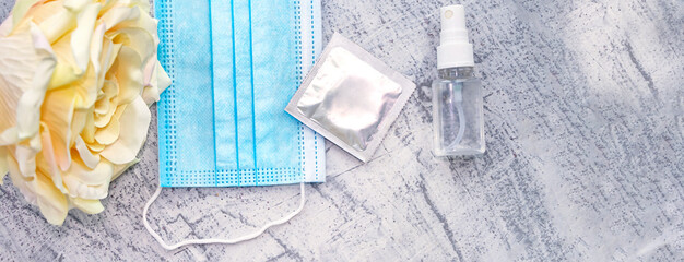 Protective medical mask, rose, condom and sanitizer on a white textured background. The concept of...