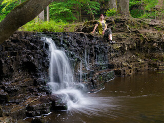 Waterfall with a small amount of water and a woman sitting on the edge of a half-dried waterfall.

Ivande waterfall with a small stream of water photographed in a long exposure, which allows the water