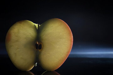 Composition with apple slices on a black background. A slice of apple with back light on a black background with water drops. Juicy apple on a table.