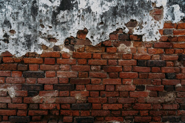 Old and worn red brick wall face with white and black cement coating peeling away.
