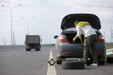Replacing the wheel of a car on the road. A man doing tire work on the sidelines.