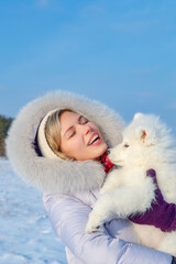 Laughing young woman and samoyed puppy kiss on winter frosty day