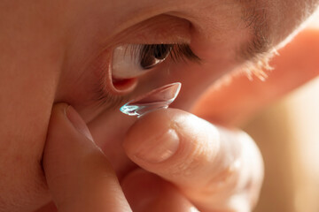 Fototapeta premium A person with poor eyesight inserts a contact lens into her eye in sunny morning