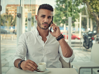 Close up of Handsome Young Man Drinking Coffee at the Shop While Looking at Cell Phone