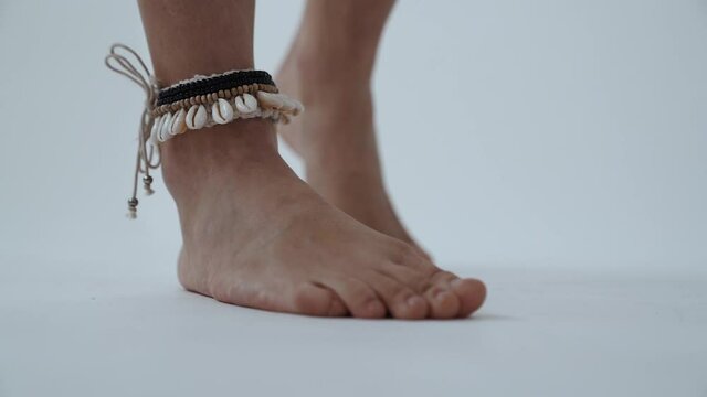 Bared Female Legs With Shells Bracelet on a White Background. Slim Young Woman Legs, Slow Motion.