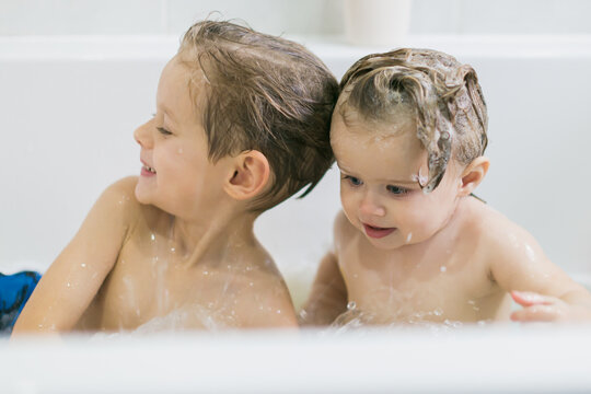 Funny little girl and her cute brother having fun taking a bath together playing in water with foam with colorful toys after a shower.