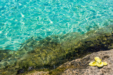 Fototapeta na wymiar View of the turquoise water in the Blue Lagoon with yellow flip flops, Comino Island, Malta