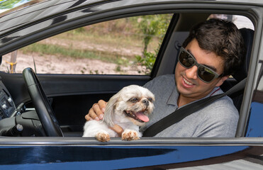 Brunette man in a black car with a seat belt wearing sunglasses and a gray polo shirt with a...