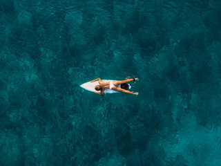 Attractive surfer woman relaxing on surfboard in ocean. Aerial view with surf girl
