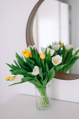 Yellow and white tulip bouquet next to mirror on dresser