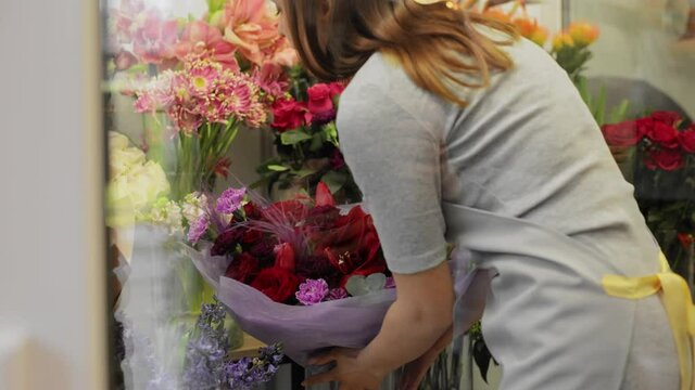 Beautiful young woman florist takes flowers from the refrigerator. Small business. Young female in apron at workplace. Florist artist taking vase with flowers from the refrigerator in flowers store.