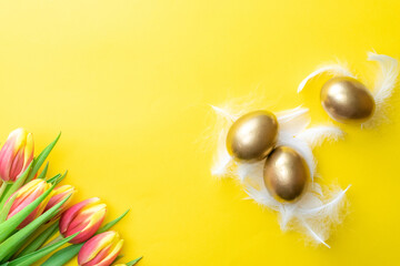 Easter eggs basket. Golden egg in basket with spring tulips, white feathers on pastel yellow background in Happy Easter decoration. Traditional decoration in sun light. Top view.