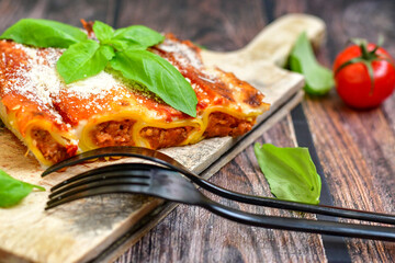 Cannelloni bolognese and parmesan cheese  on a wooden rustic  background.Home made italian meal
