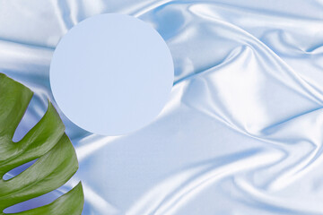 Geometric platform podium and monstera leaf on pastel blue silk satin background. Blank minimal...