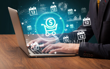 Business hand working on laptop with shopping cart with dollar icons coming out from the screen, successful business concept