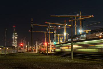 Langzeitbelichtung Zug verlässt die Station in der Nacht. Im Hintergrund Kräne einer Baustelle...