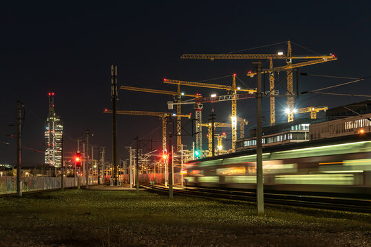 Langzeitbelichtung Zug verl&auml;sst die Station in der Nacht. Im Hintergrund Kr&auml;ne einer Baustelle und ein Wolkenkratzer. Zugsignale in rot und gr&uuml;n.  