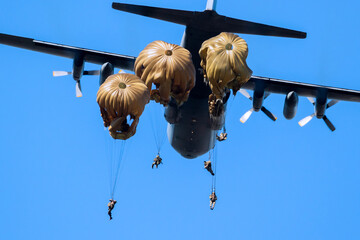 Military parachutist paratroopers parachute jumping out of a air force planes on a clear blue sky day.