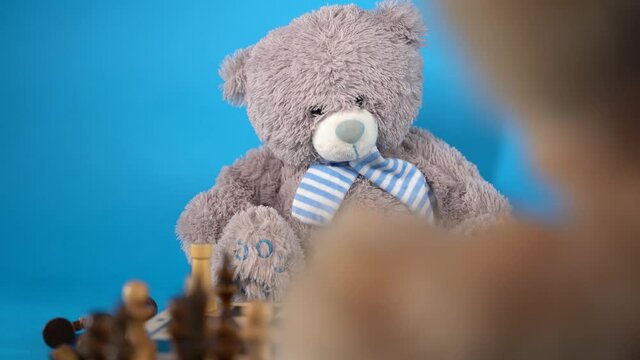 Close up of teddy bears with chess pieces on chessboard. Soft plush toys playing chess on blue background.