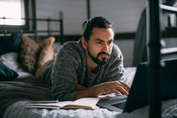 Young man lies on bed with laptop at home